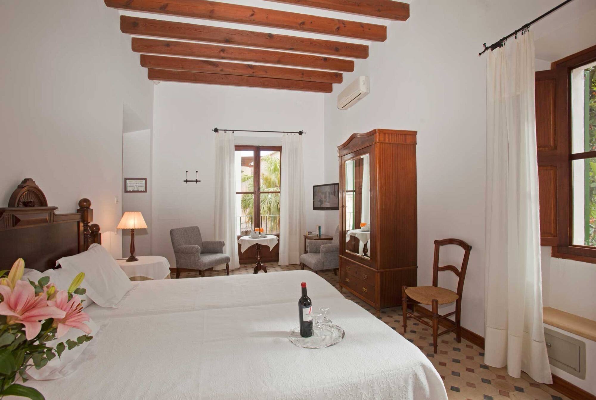 A room with a beamed ceiling, a dark-wood wardrobe and grey armchairs by a curtained window.