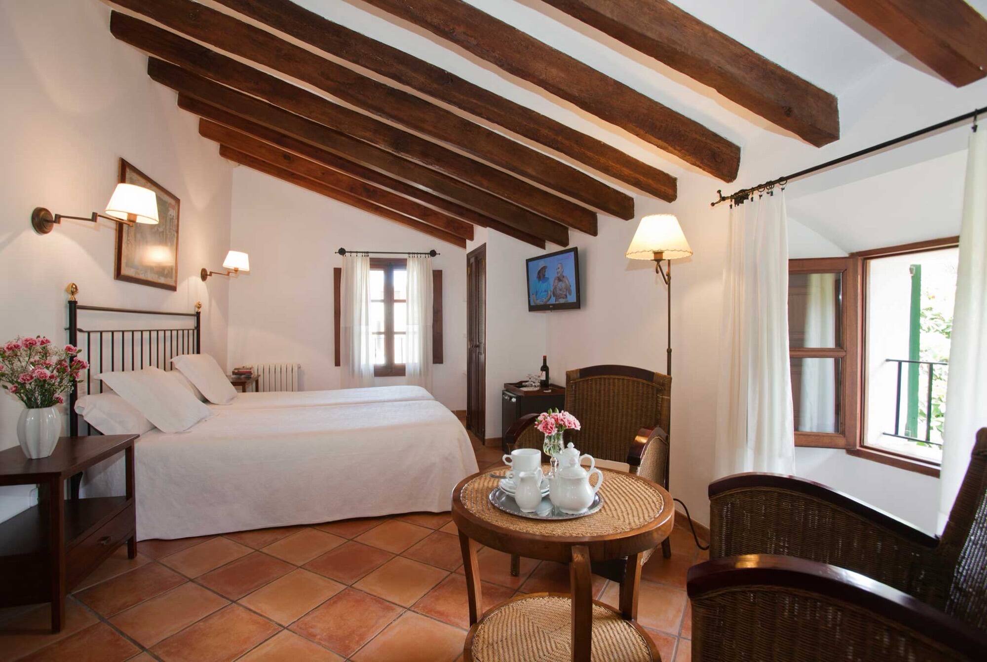 A room with dark exposed beams, an iron bed and a breakfast tray on a round table by the window.