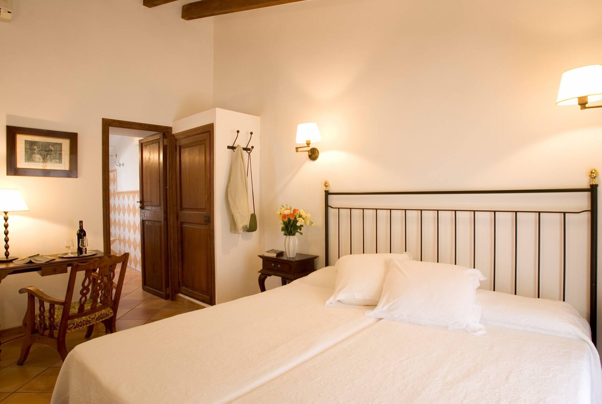A room with a wrought-iron bed, a small writing desk laid for two and fresh flowers.